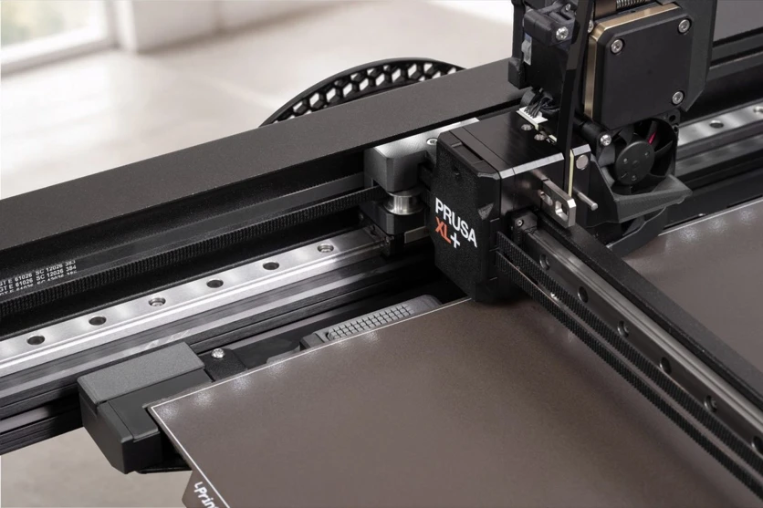 The XL+ toolhead over the front edge of the bed, where the wiper strip and the tool offset sensor now sit (Prusa Research)